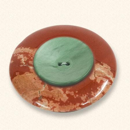 Ein Trauerknopf aus Jaspis mit einem grünen Knopf eines geliebten Menschen darauf. Der rote Jaspis ist oft geädert.